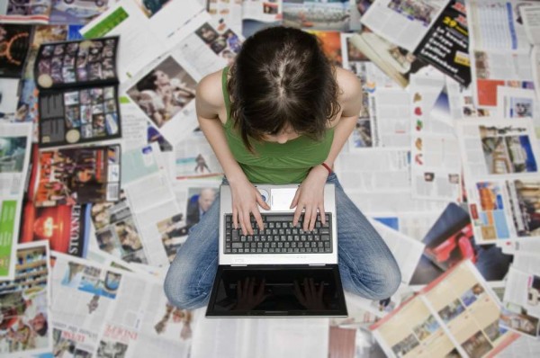 girl with a laptop sitting on newspapers