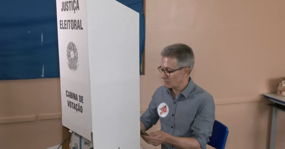 Romeu Zema segura celular diante da urna eletrônica